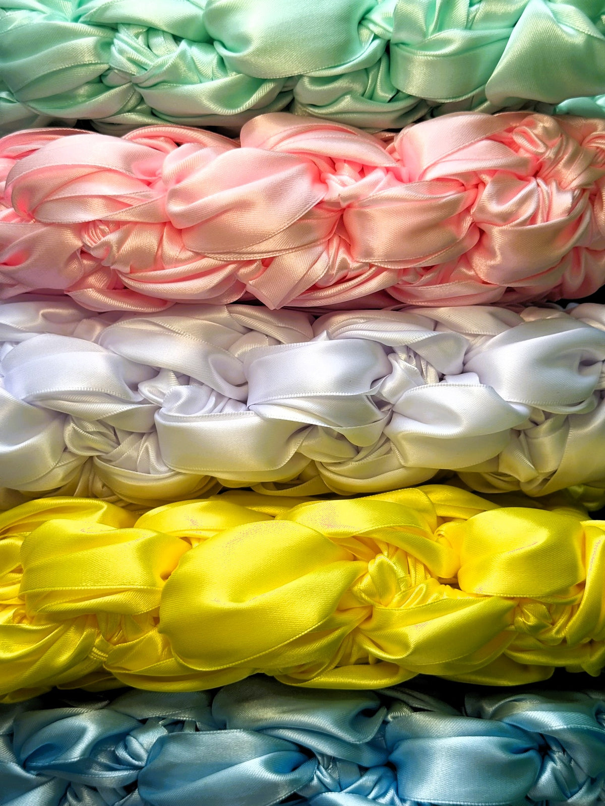 Stack of colourful satin ribbon crocheted in pink, white, yellow, green, and blue.