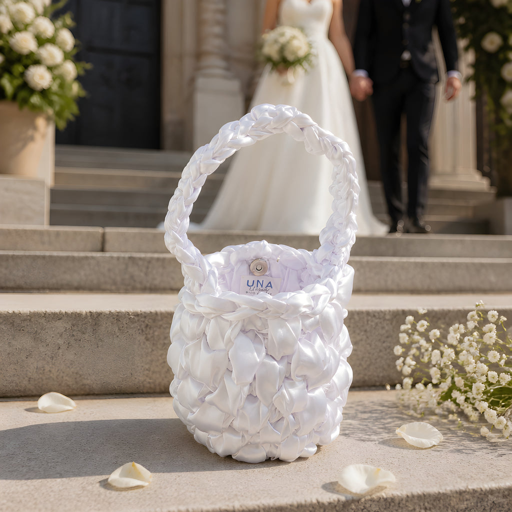 White BRIDAL CROCHET BAG With 'UNA' branding on steps with a blurred wedding couple in the background.