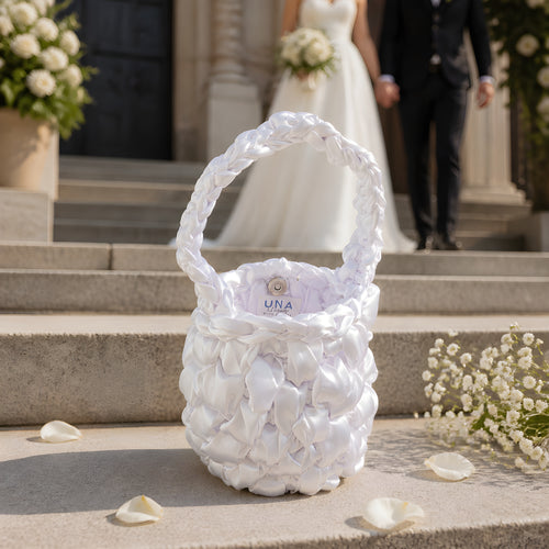 White BRIDAL CROCHET BAG With 'UNA' branding on steps with a blurred wedding couple in the background.