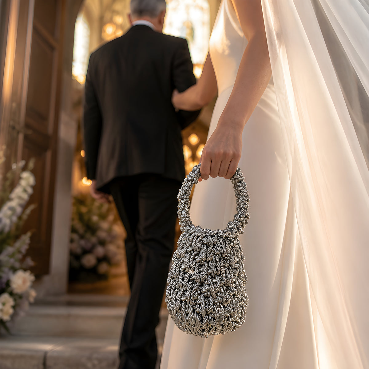 Bride holding a silver-textured crochet handbag against a blurred background of a couple walking together.