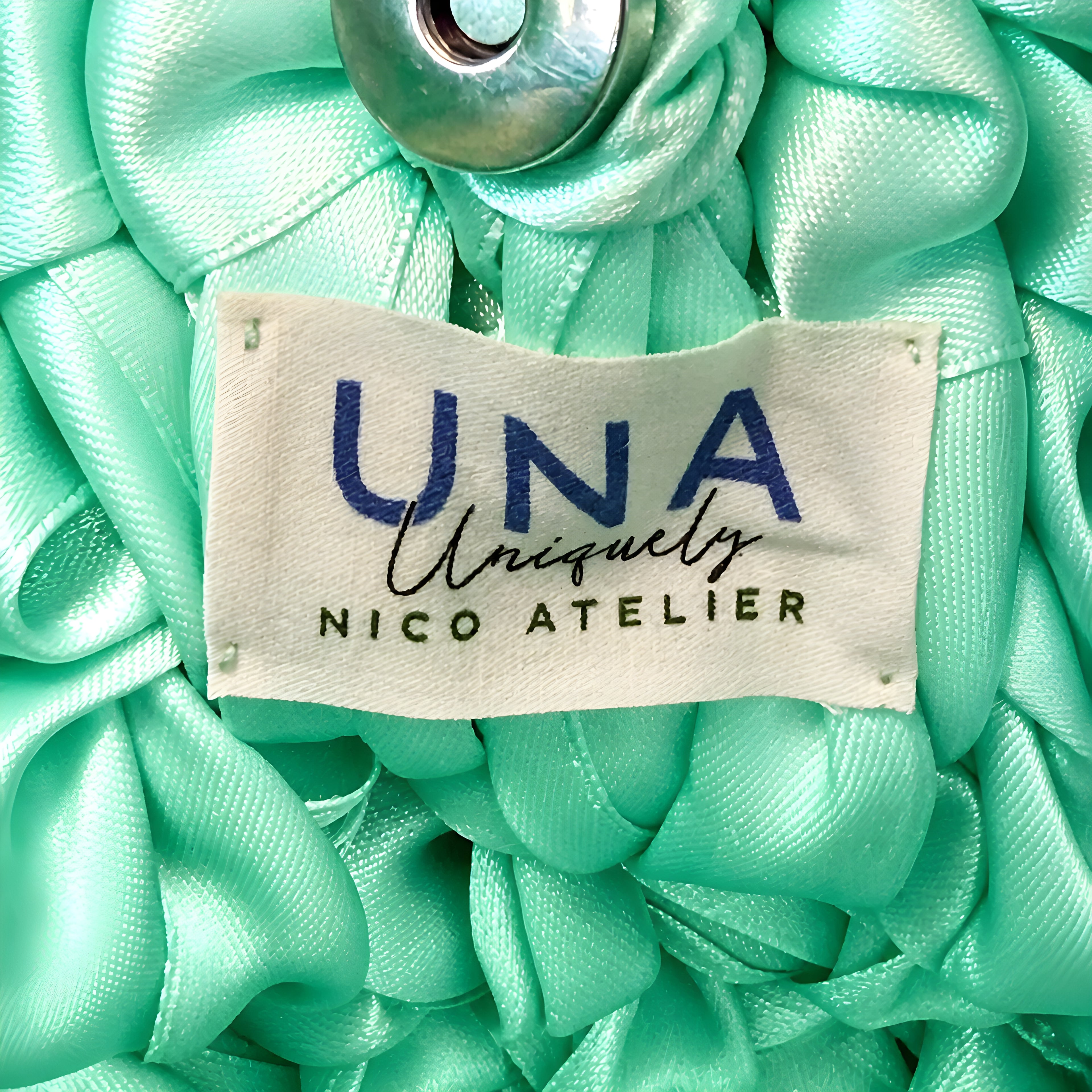 Close-up of mint green SATIN CROCHET BAG with a 'UNA uniquely NICO ATELIER' label.
